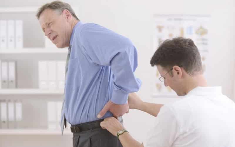 man holding back while getting checked by a chiropractor