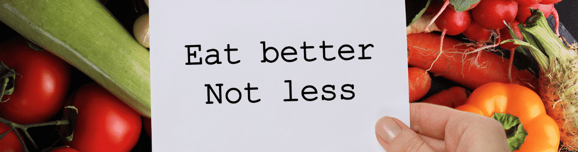 person holding a sign over some vegetables that says to eat better not less